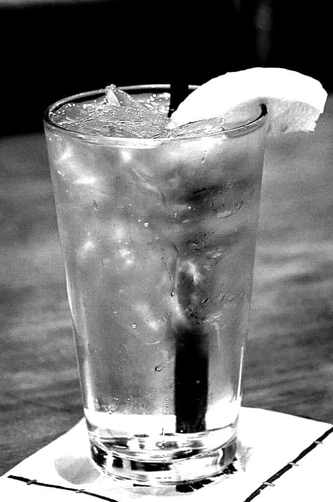 A glass of ice water with straw and a lemon slice.